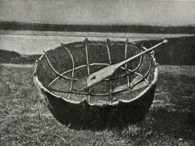 A small circular boat, pulled on shore, with one oar resting inside.